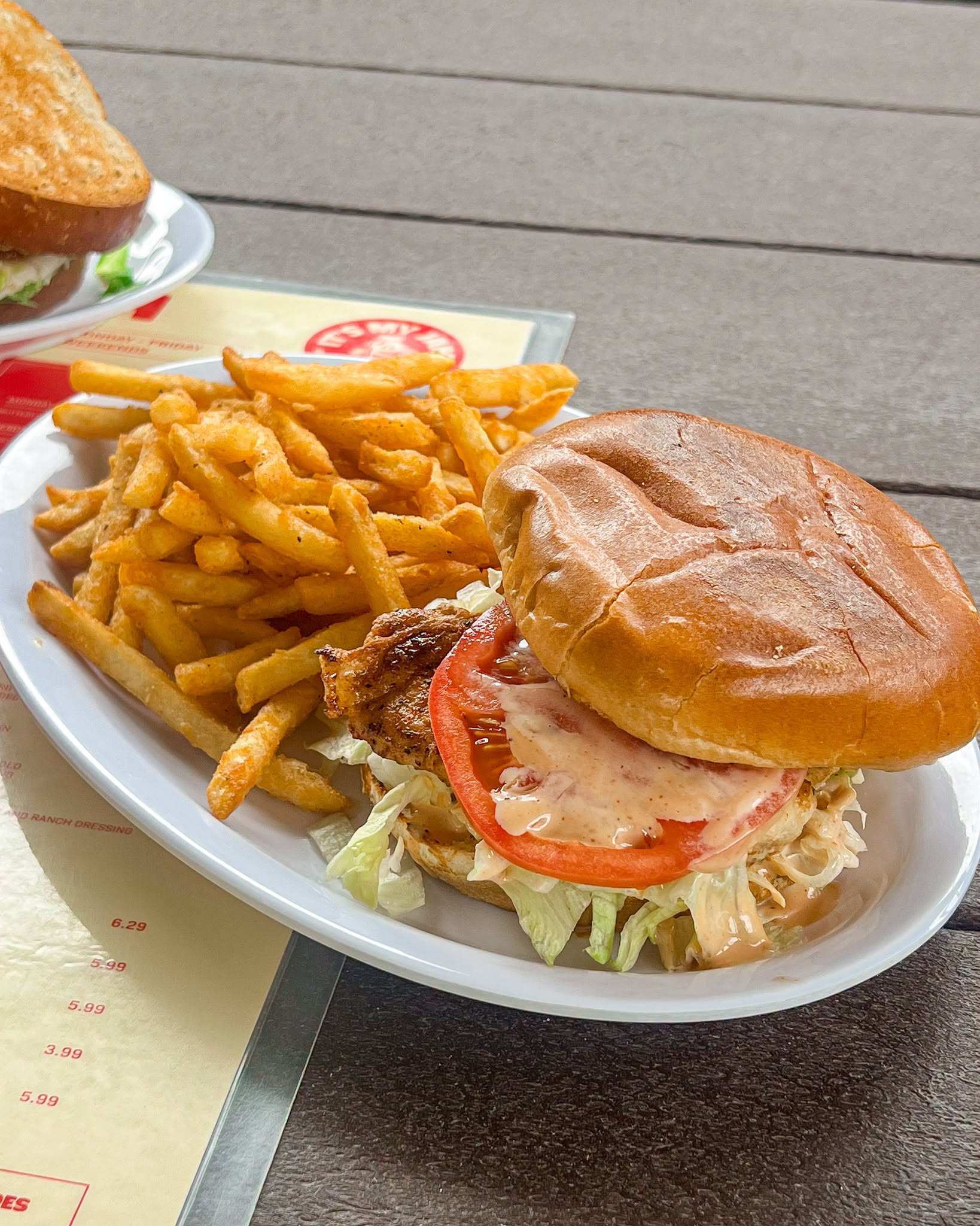 Chicken sandwich with lettuce, tomato, sauce, and fries served on a white plate at It’s My Jam Cafe.
